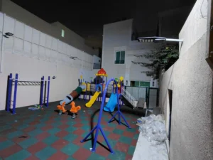 Backyard outdoor playground in Saudi Arabia with slides, climbing equipment, spring riders, swing frame, and rubber flooring
