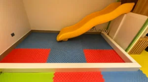 Indoor kids yellow slide with shock absorbing flooring mat in a children’s play area.