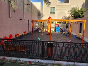 Outdoor kids play area in a Saudi villa with swings, slides, climbing features, benches, and rubber safety flooring