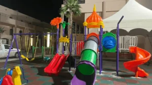Outdoor kids’ play tower with tunnel slide, spiral slide, double straight slide, swings, and rubber safety flooring in Saudi Arabia.