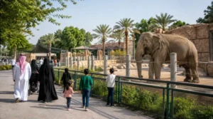 A realistic travel photograph of Riyadh Zoo in Al Malaz, Riyadh, Saudi Arabia, showing Saudi families exploring the zoo and viewing animals like elephant in landscaped animal habitats.