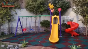 Residential playground in Dammam with swings, straight slide, spiral slide and red and green rubber tile flooring, installed by Ebaza Gardens.