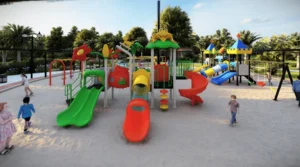 Colorful outdoor playground with slides, tube slide, climbing frames, and swings on sand surface in a park setting