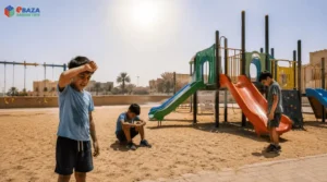 Tired children near an unshaded outdoor playground under strong Saudi summer heat with open play equipment and direct sun exposure.