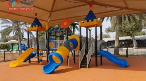 Shaded outdoor playground equipment in Saudi Arabia with slides, tunnel slide, climbing structure, rubber safety flooring, and Ebaza Gardens logo.