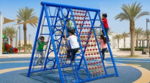 Children climbing on a blue double-sided playground monkey bar with rope net, circular climbing rings, side ladders, and safety flooring.