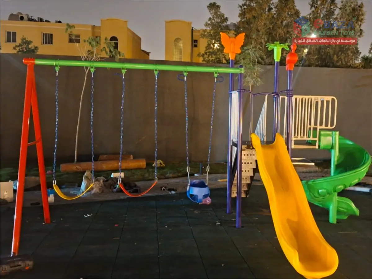 Kids playground installation with swing set, yellow slide, green spiral slide, raised platform, stairs, and rubber flooring.
