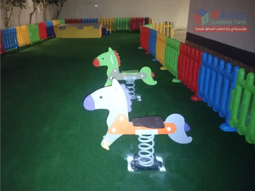 Two horse-shaped children’s spring riders on artificial grass inside a fenced play area.
