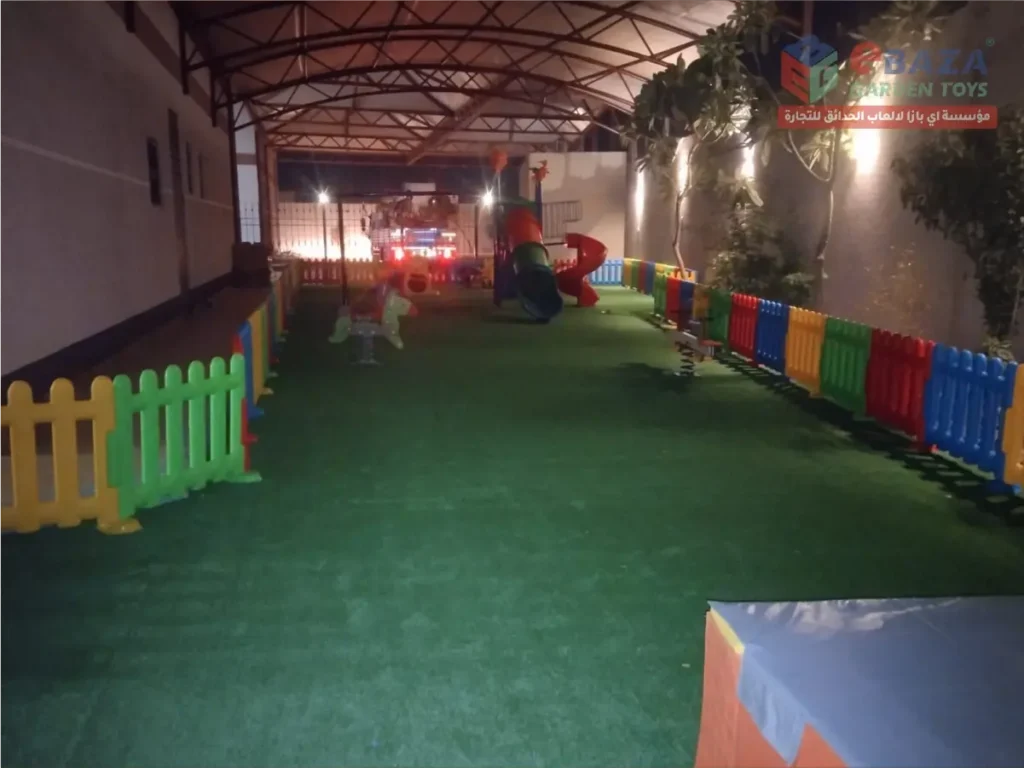 Covered children’s playground with colorful fencing, artificial grass, slides, and spring play equipment.