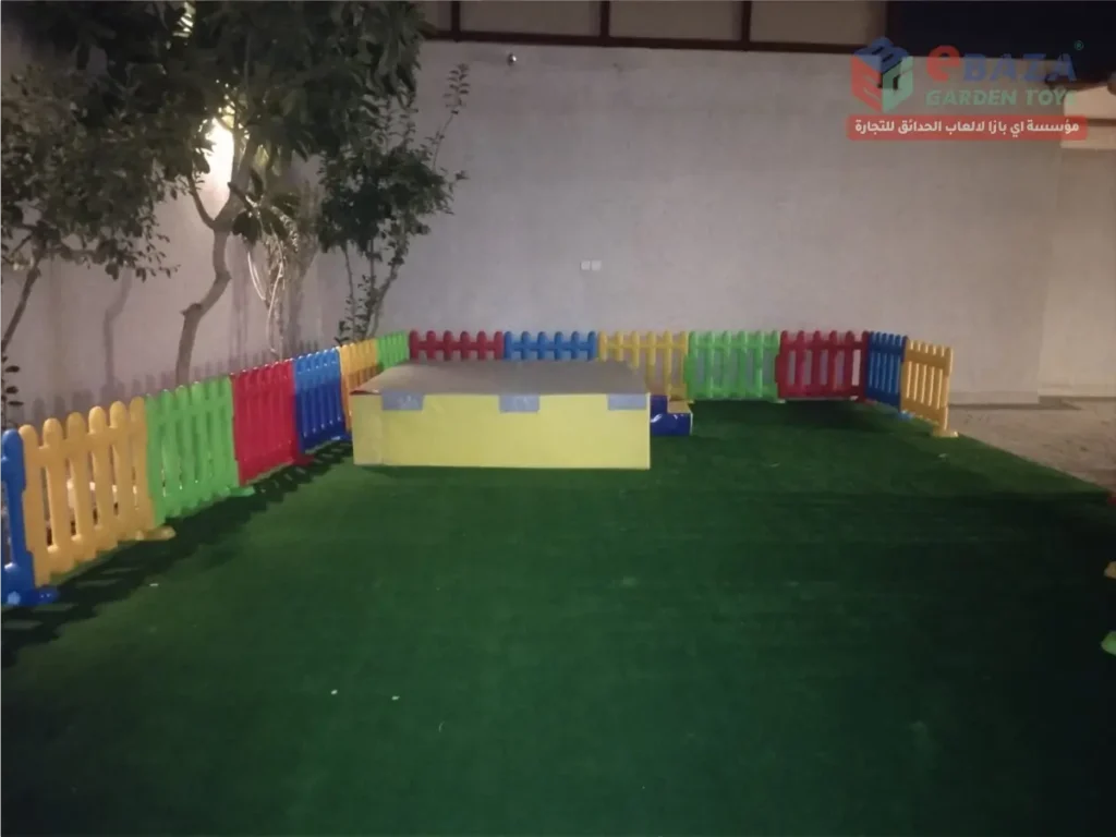 Fenced children’s play area with artificial grass and a padded soft-play platform.