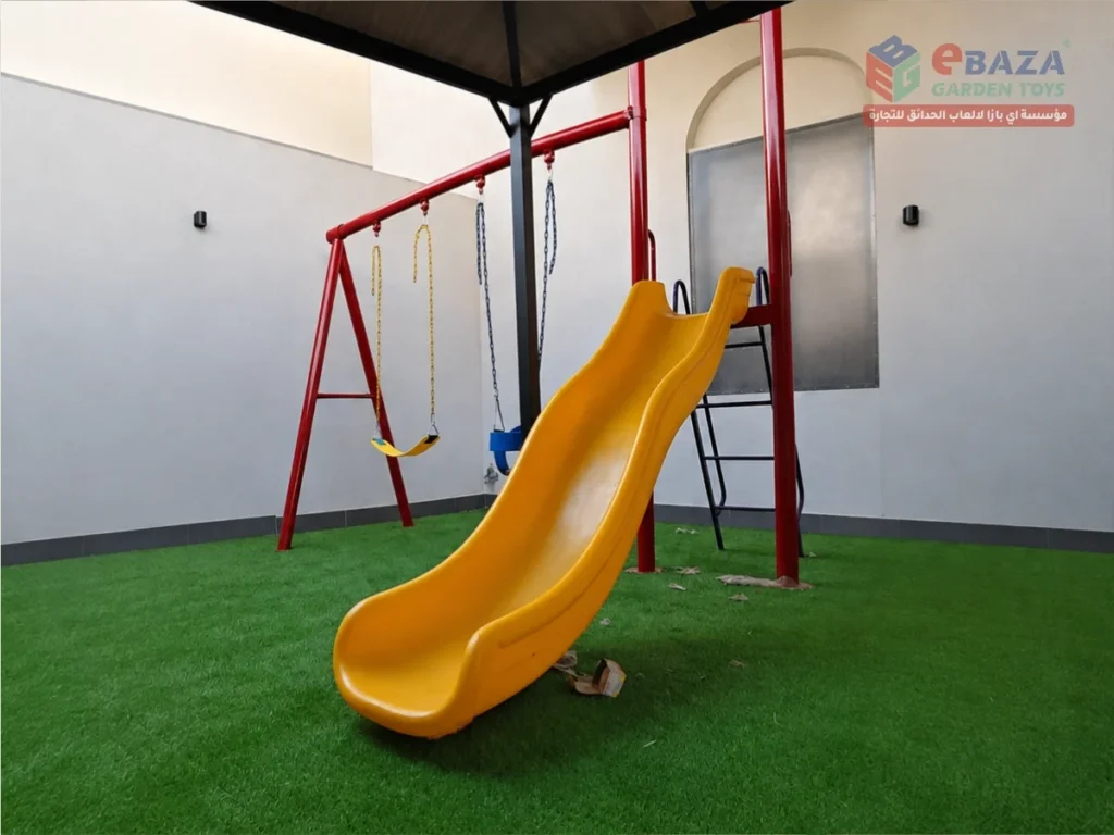 Outdoor playground in Jeddah with yellow slide, two-seat swing set and artificial grass flooring.
