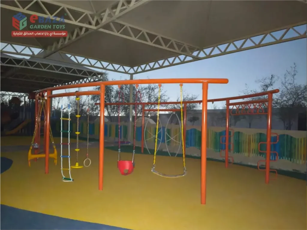 Outdoor playground installation in Al Kharj with kids’ swings, rope ladder, gym ring, overhead climbing bars and shaded safety flooring.