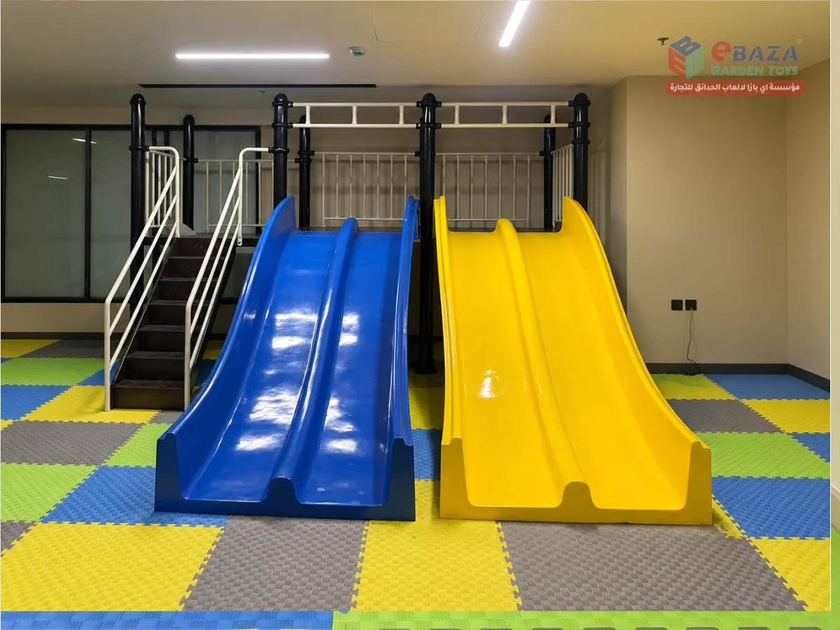 Indoor playground installation Riyadh with blue and yellow double slides, stairs, elevated platform and foam safety flooring at Alfanar.