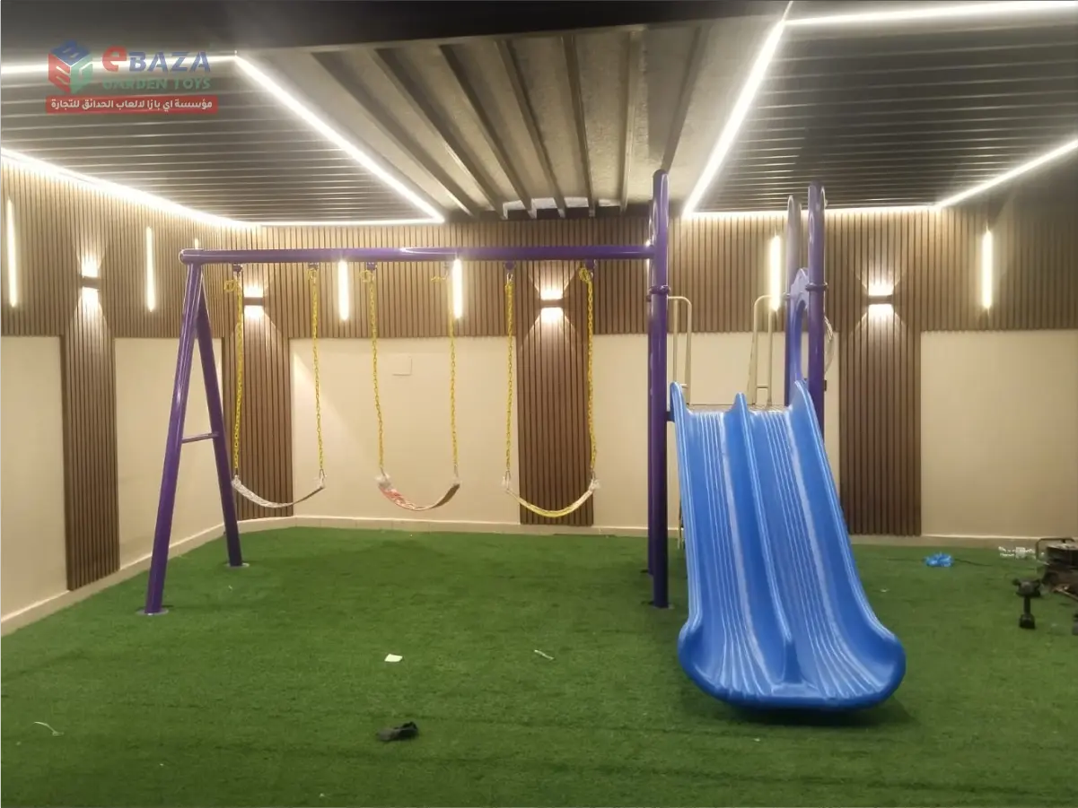 School playground installation in Shubra, Riyadh with three-seat swings, blue double slide and artificial grass flooring.